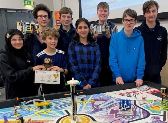 A group of eight students stand behind a table with Lego on it after winning a tournament