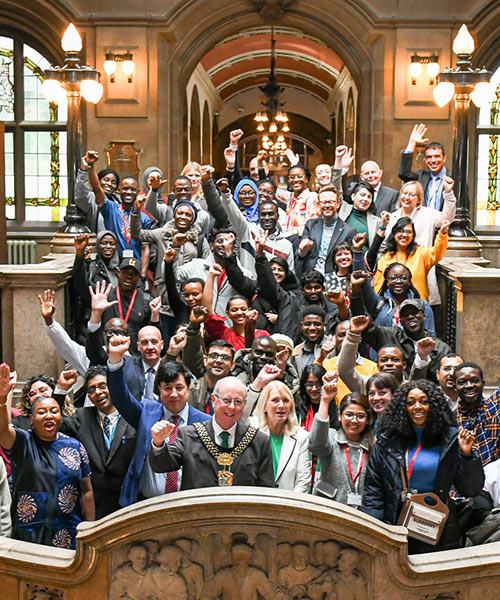 International students standing on the stairs smiling with fists raised at Bradford City Hall for the Lord Mayors' reception