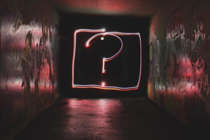Neon sign of a question mark inside a box in a dimly lit corridor.